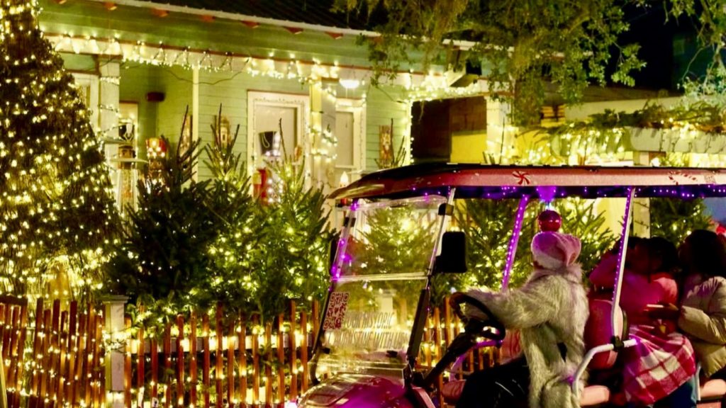 Pink golf cart tour driving past decorated holiday home in St. Augustine’s Nights of Lights