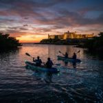 Four kayakers paddling on water glowing with bioluminescent light near castillo de san marcos in ST. Augustine, Florida on a bioluminescence tour